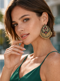 Woman wearing large, ornate earrings with a blurred outdoor background